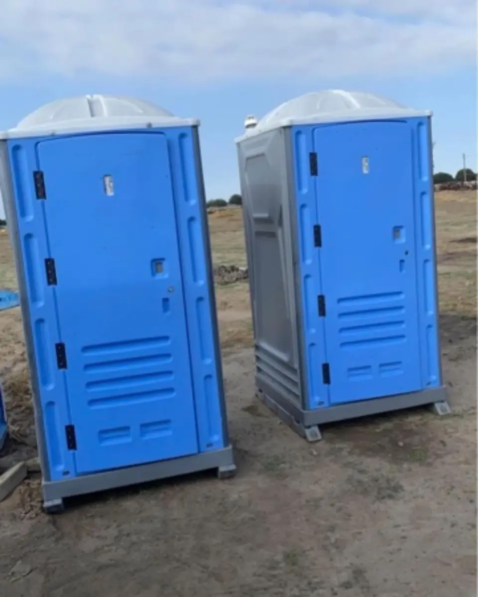 Two blue standard porta potties on a dirt lot